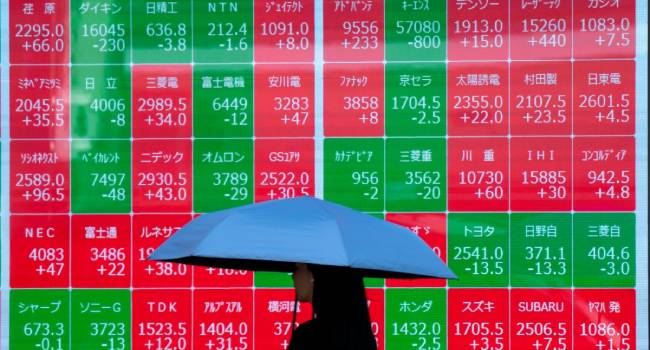 A woman walks past an electronic board showing the Nikkei 225 index on the Tokyo Stock Exchange in Tokyo on June 17, 2025. (Photo by Kazuhiro NOGI / AFP)
